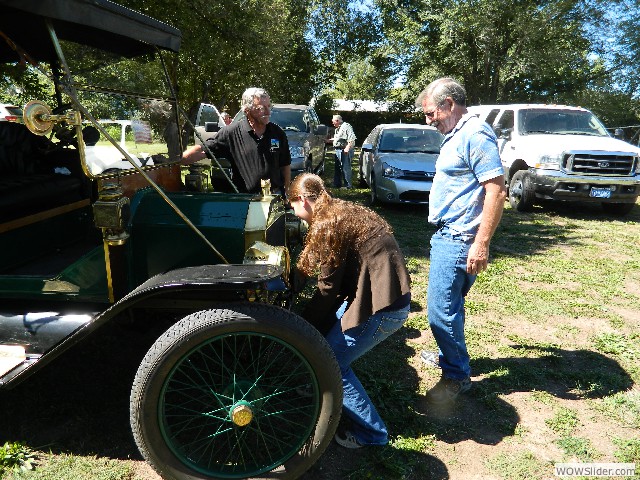 Larry instructing Faith Carmody how to start a Model T while grandfather Gerald looks on